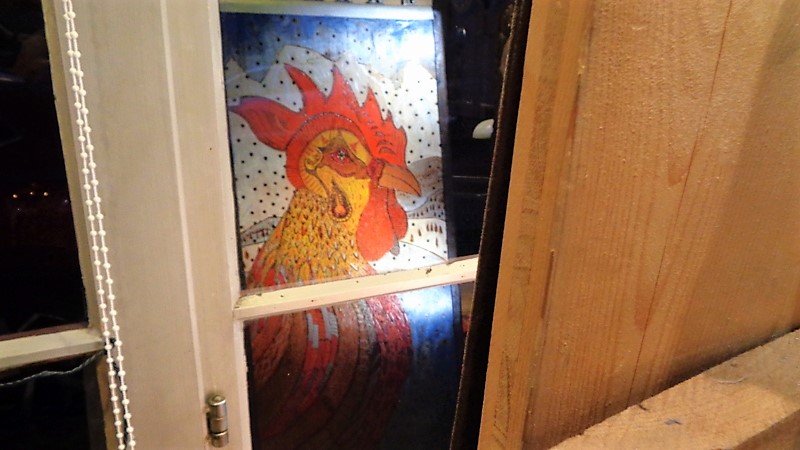 11. Un coq en pyrogravure et peinture se reflète dans la vitrine